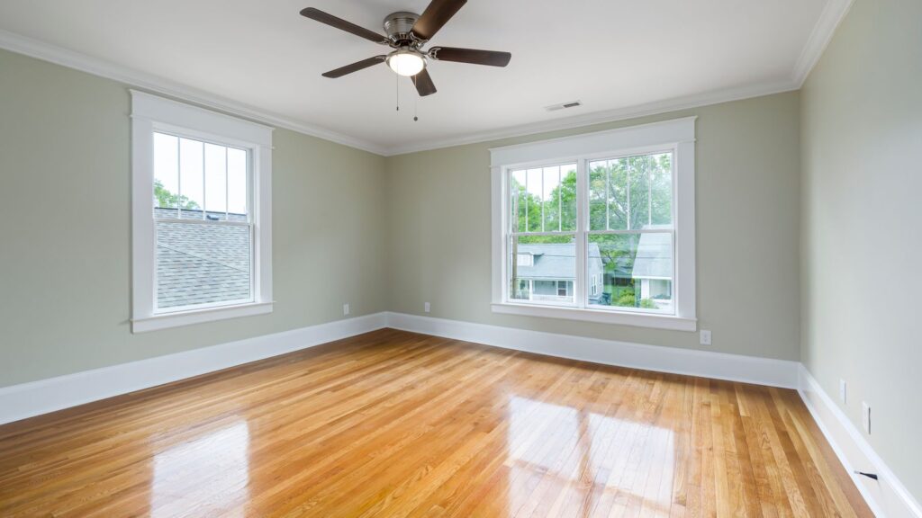 Bright empty room with wooden floors, large windows, and a ceiling fan.