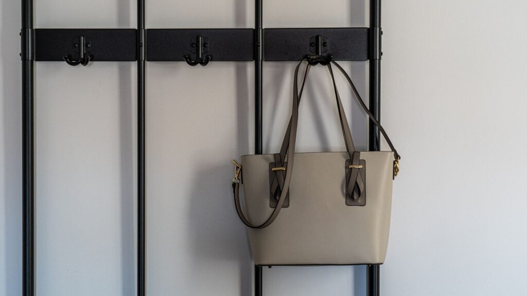 Stylish grey leather purse with gold details hanging on a modern black hook against a minimalist backdrop.