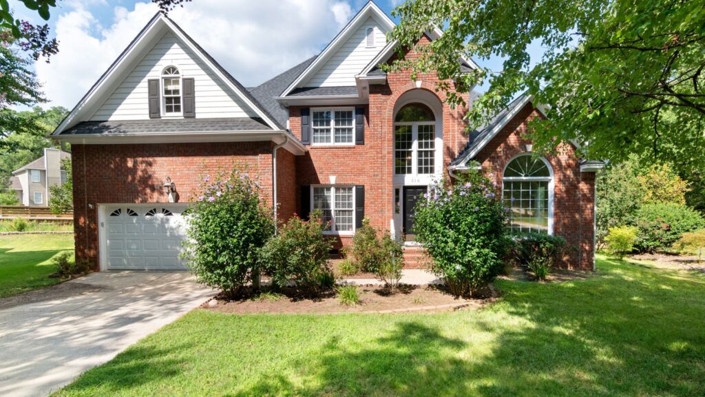 Charming two-story brick house in sunny suburb with lush front lawn.