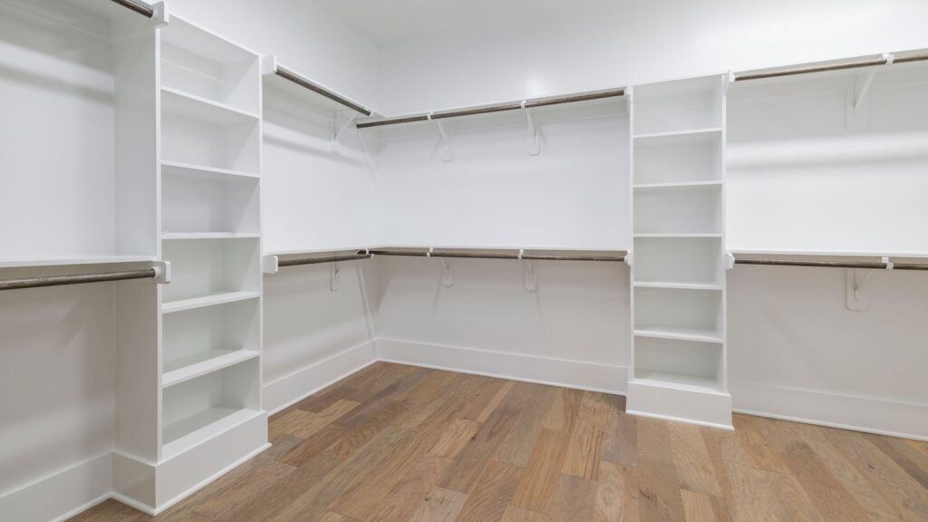 Empty modern walk-in wardrobe featuring wood floors and white shelving.