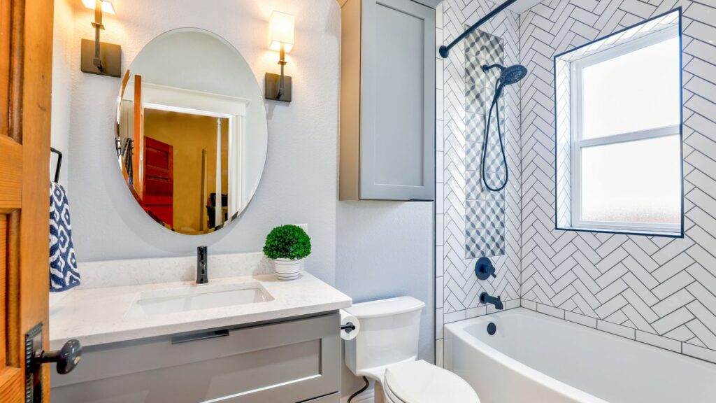Elegant modern bathroom featuring chevron tiles, oval mirror, and sleek fixtures for a contemporary look.